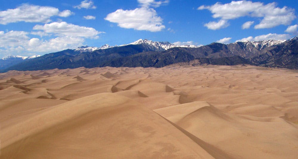 Wavy hills of sand stretch out towards the base of tree- and snow-covered mountains at the Great Sand Dunes National Park and Preserve in western Colorado.