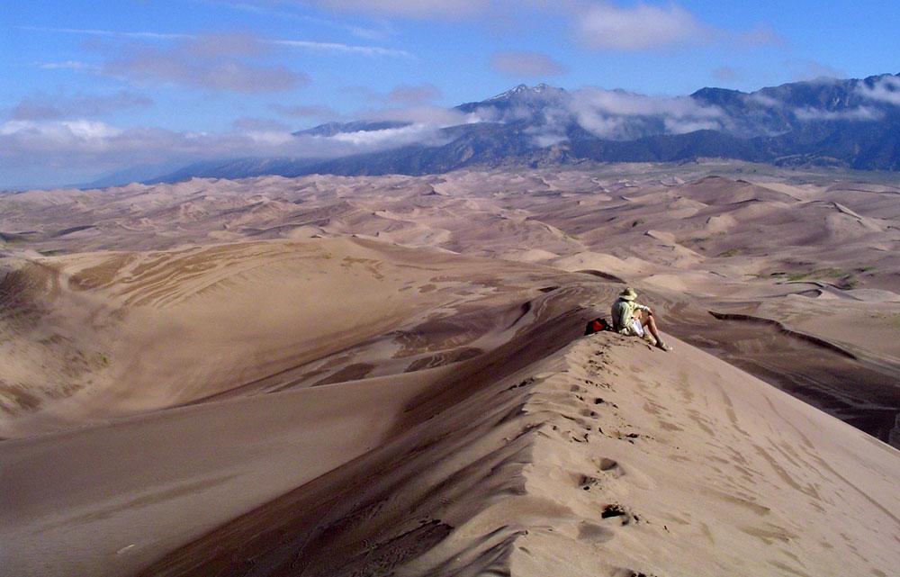 A person sitting on a massive dune over Great Sand Dunes National Park and Preserve