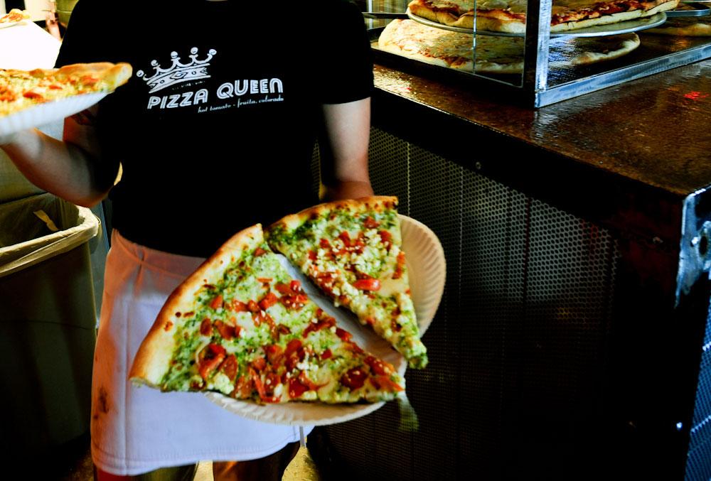 A server holds two colorful slices of the Granny's Pesto Pizza on plates at The Hot Tomato in Fruita, Colorado.