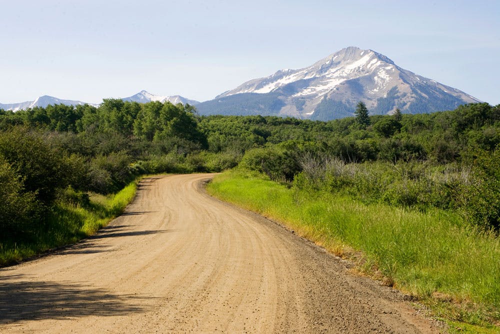 A dirt road in natural surroundings with a towering snow-capped mountain in the background