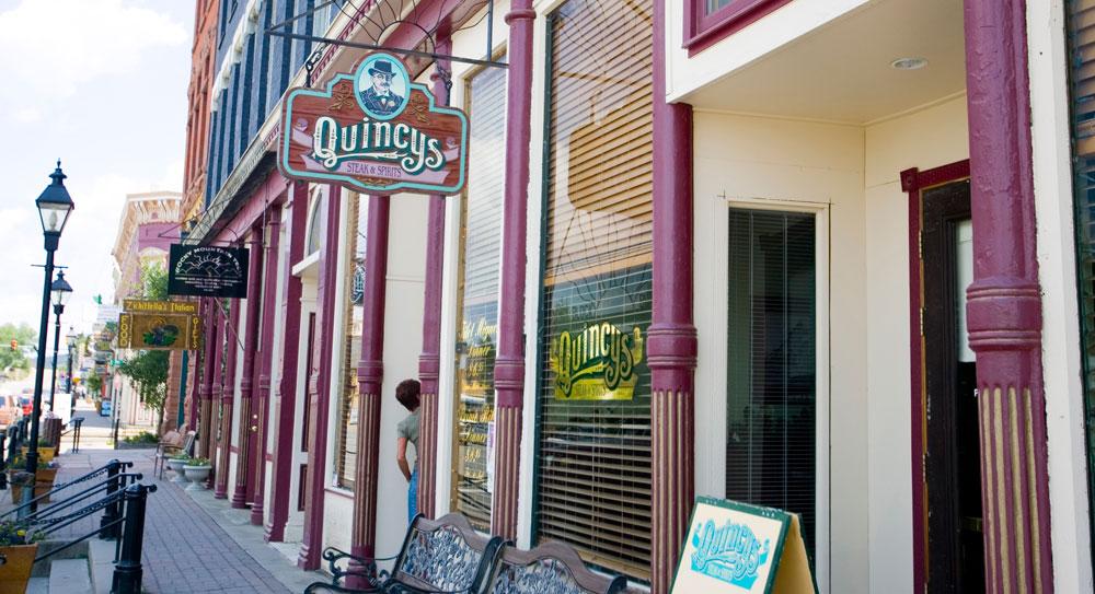 A row of Victorian-era shops and restaurants; a sign for Quincy's hangs on a wooden board