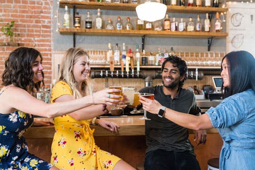 Four friends cheers their beers at the bar of a brewery