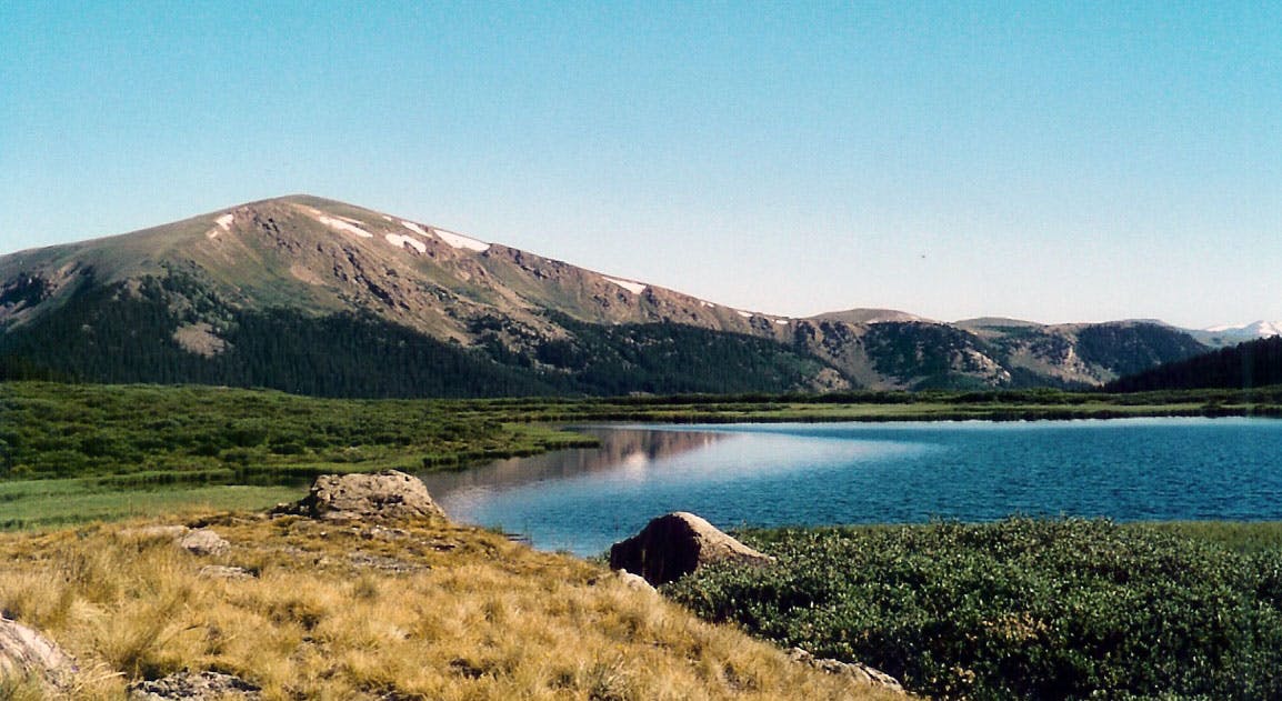 Grey Mount Bierstaat, with a few patches of snow, sits next to a blue lake and field of grass