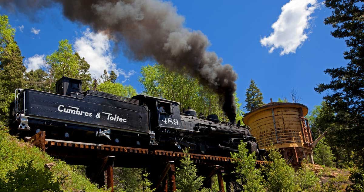 A train on the Cumbres & Toltec Scenic Railroad in Antonito chugs along with black smoke coming out of the top