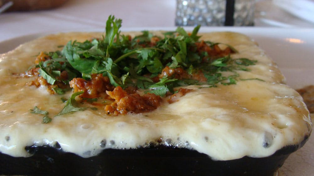 A portion of bubbling, melty cheese is lopped with crispy bits of bacon and sprigs of fresh, verdant cilantro at Tamayo in Denver, Colorado.