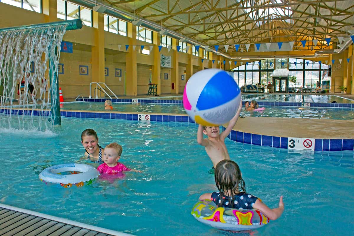 Two children toss a beach ball back and forth while a woman swims with a toddler near a life ring at the indoor Salida Hot Springs Aquatic Center.