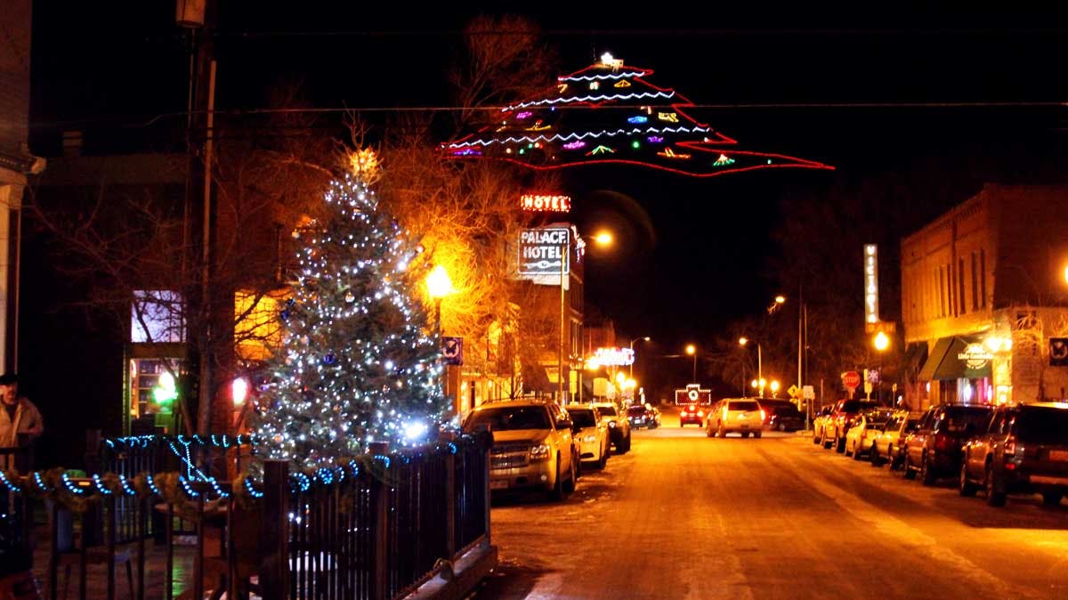 On a dark night, a flat-lay light display showcases a Christmas tree atop a mountain in the distance. In the foreground, a Christmas tree is lit on a patio.