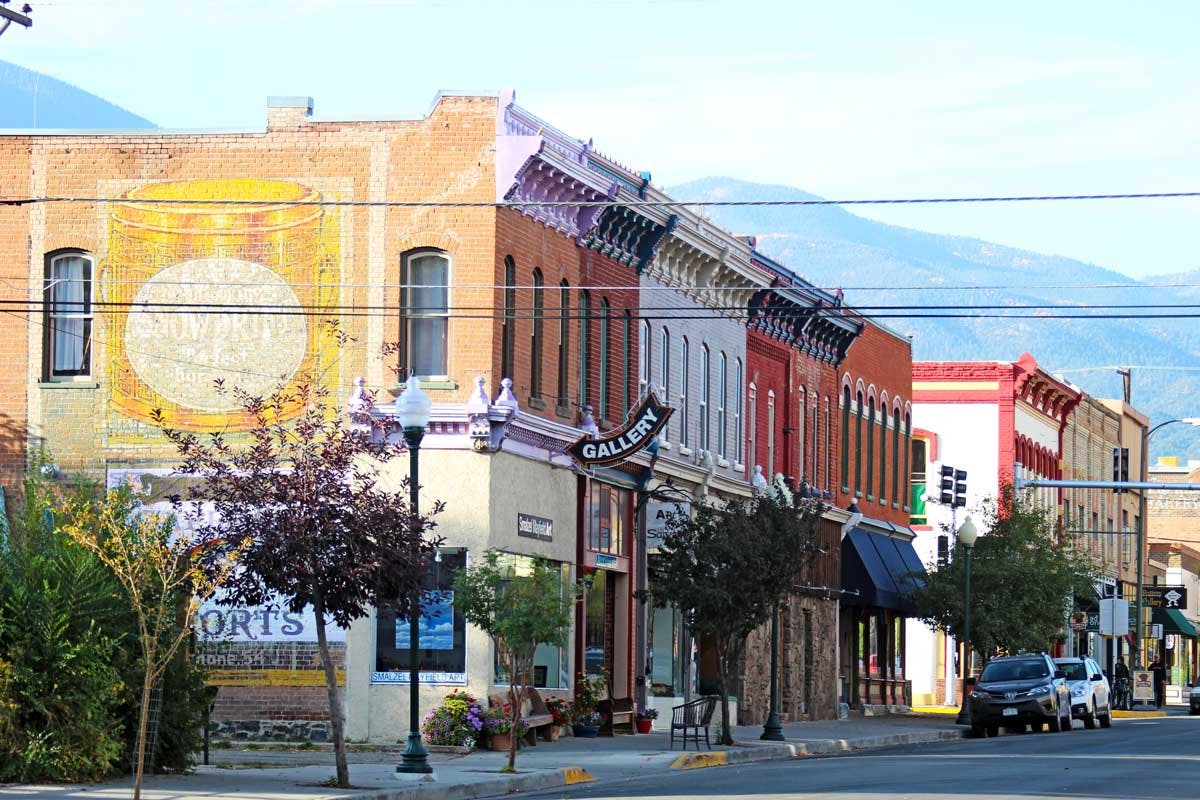 Two-story brick buildings sit on the side of a street with cars parked parallel.