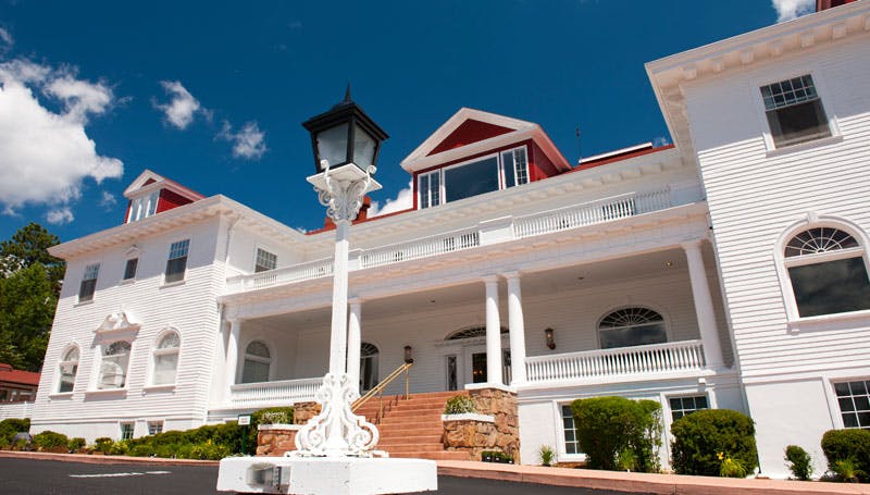 The front of the Stanley Hotel in Estes Park welcomes guests with a wide, red-stone staircase leading up to it white columned porch.