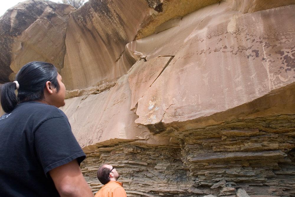 A Ute guide looks up at the step, redrock cliff wall