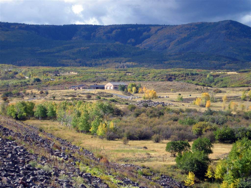 In the shadow of a tree colored hill, we see buildings, trees and a rocky trail populate a peaceful valley