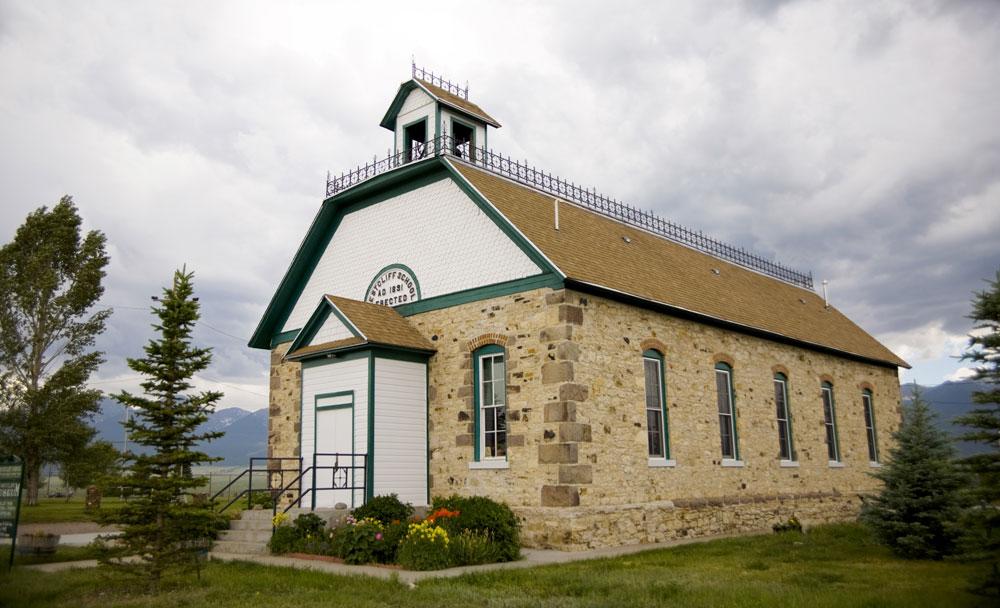 A well-preserved, brick one-room schoolhouse with flower bushes in front