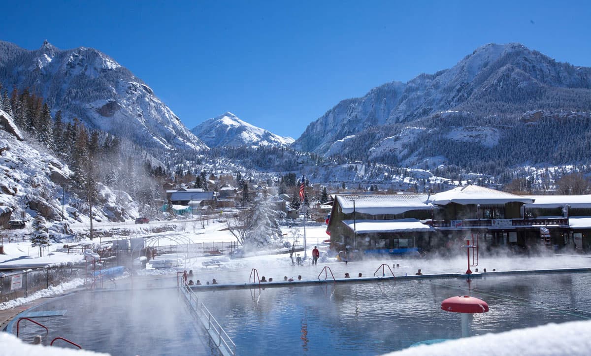 Ouray Hot Springs Pool in Winter. The sun is shining and sky is blue, but snow carpets the ground