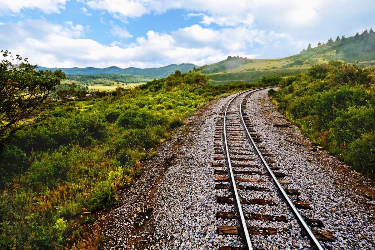 An empty railroad track stretches across a mountain landscape