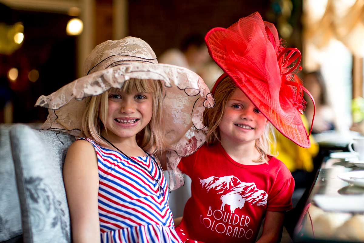 Two children wear wide-brimmed fancy English-style hats and pose for the camera at a high tea session in Colorado.