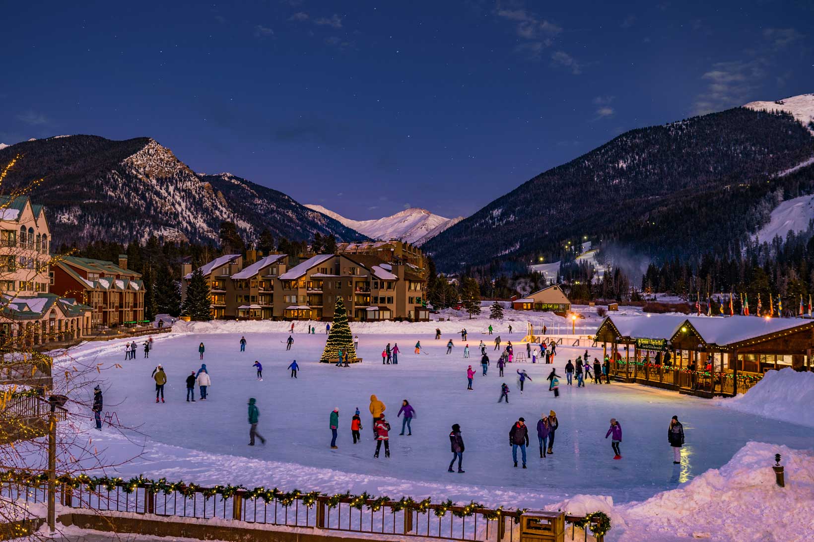 As the sun sets, a large group of people circle an ice rink in a ski town village