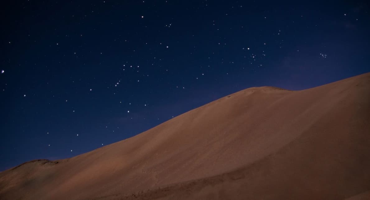 Star-filled sky above a large, tan sand dune