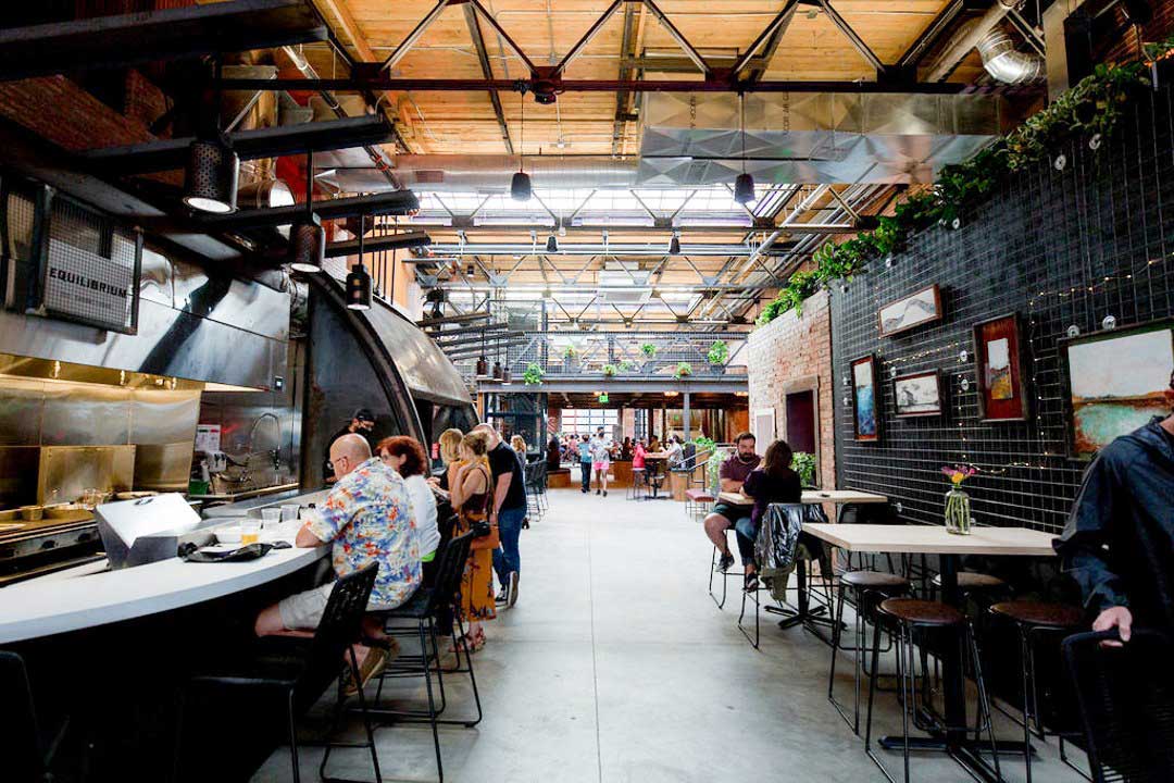 Diners sit at a bar and tables inside a industrial-styled food hall