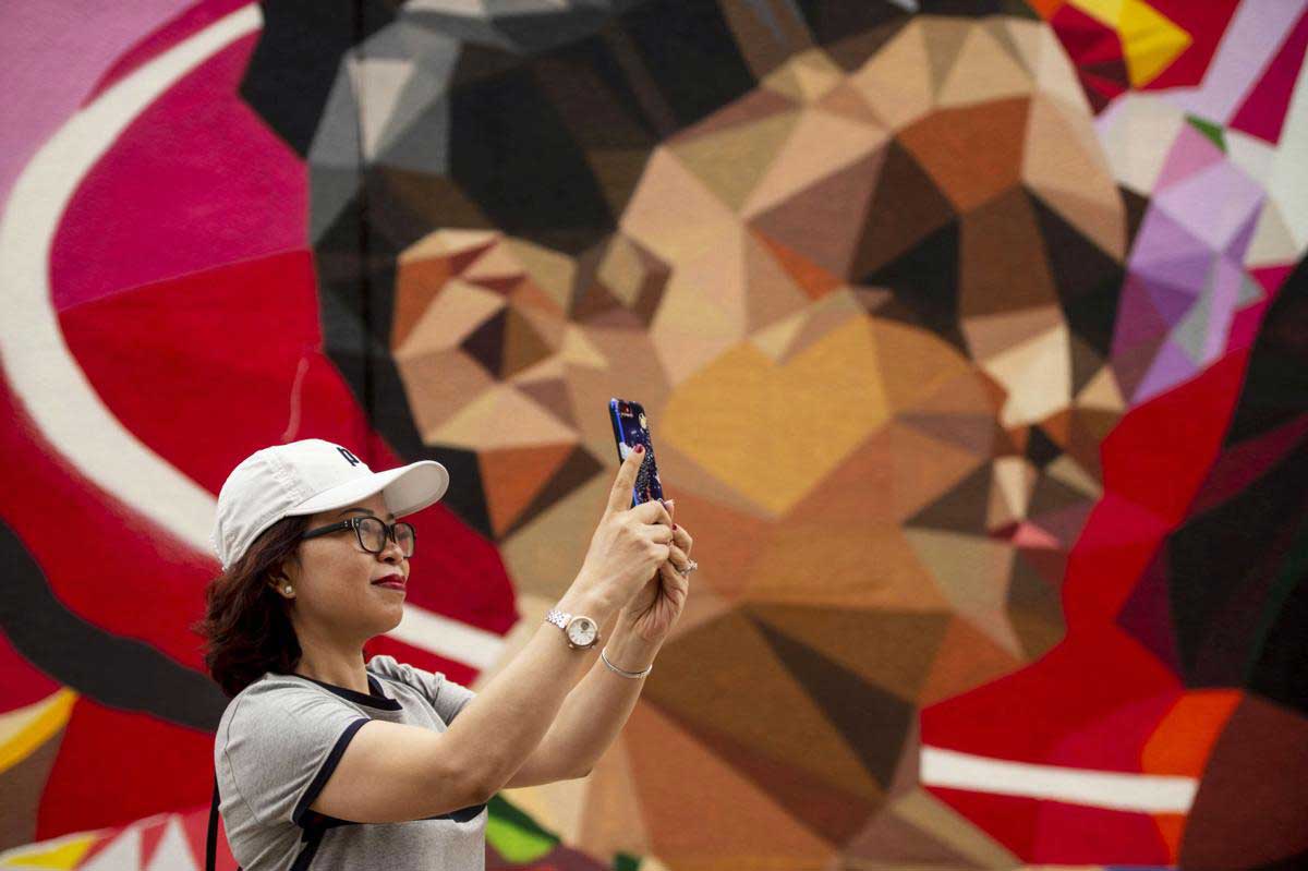 A woman stands in front of a mural taking a picture