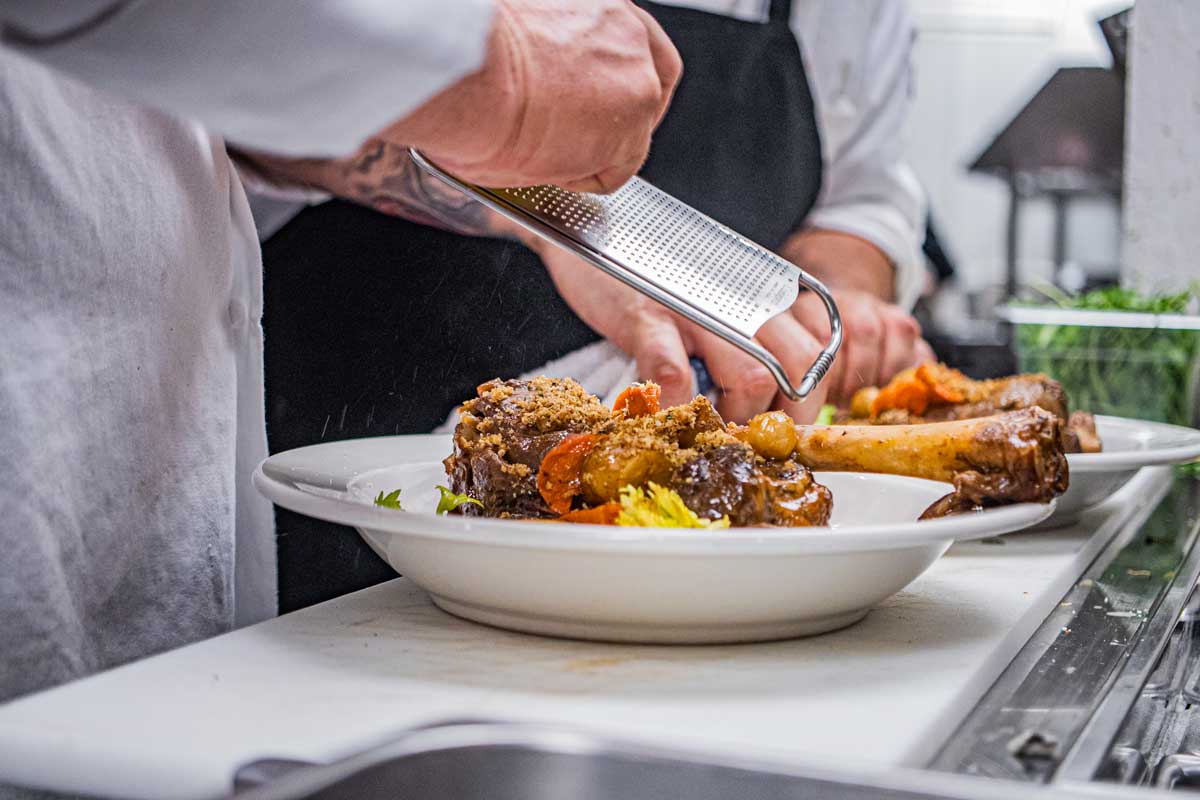 The hands of two chefs in white coats grate cheese over dishes