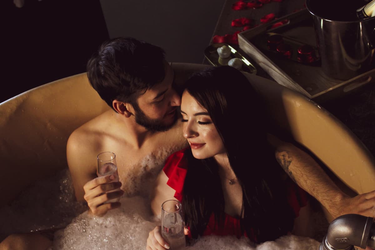 A couple sits in the beer bath hydrotherapy at Oakwell Beer Spa, leaning against each other and smiling with champagne glases in their hands.