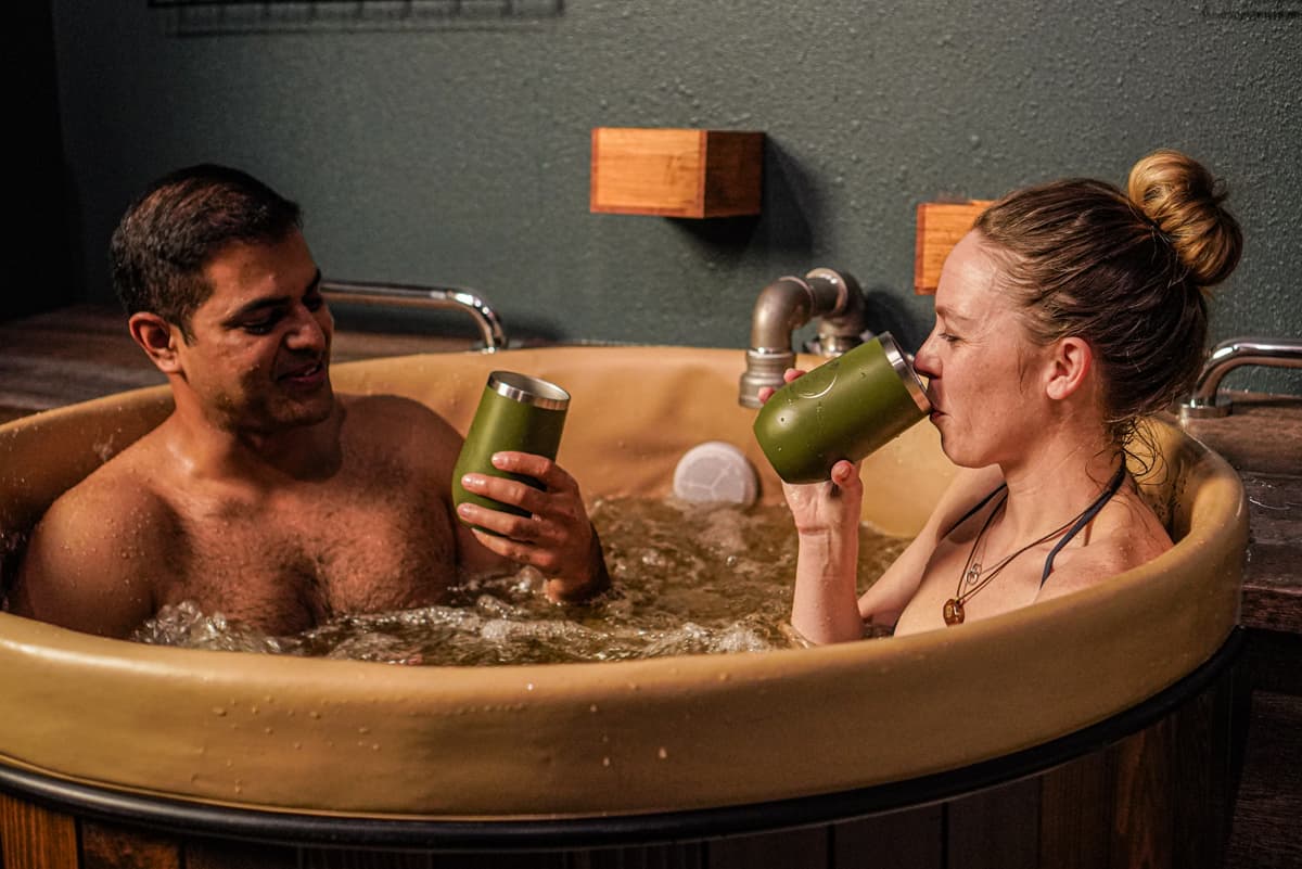 Two people sit in the beer bath hydrotherapy sipping on beer in their dark-green tumblers at Oakwell Beer Spa.