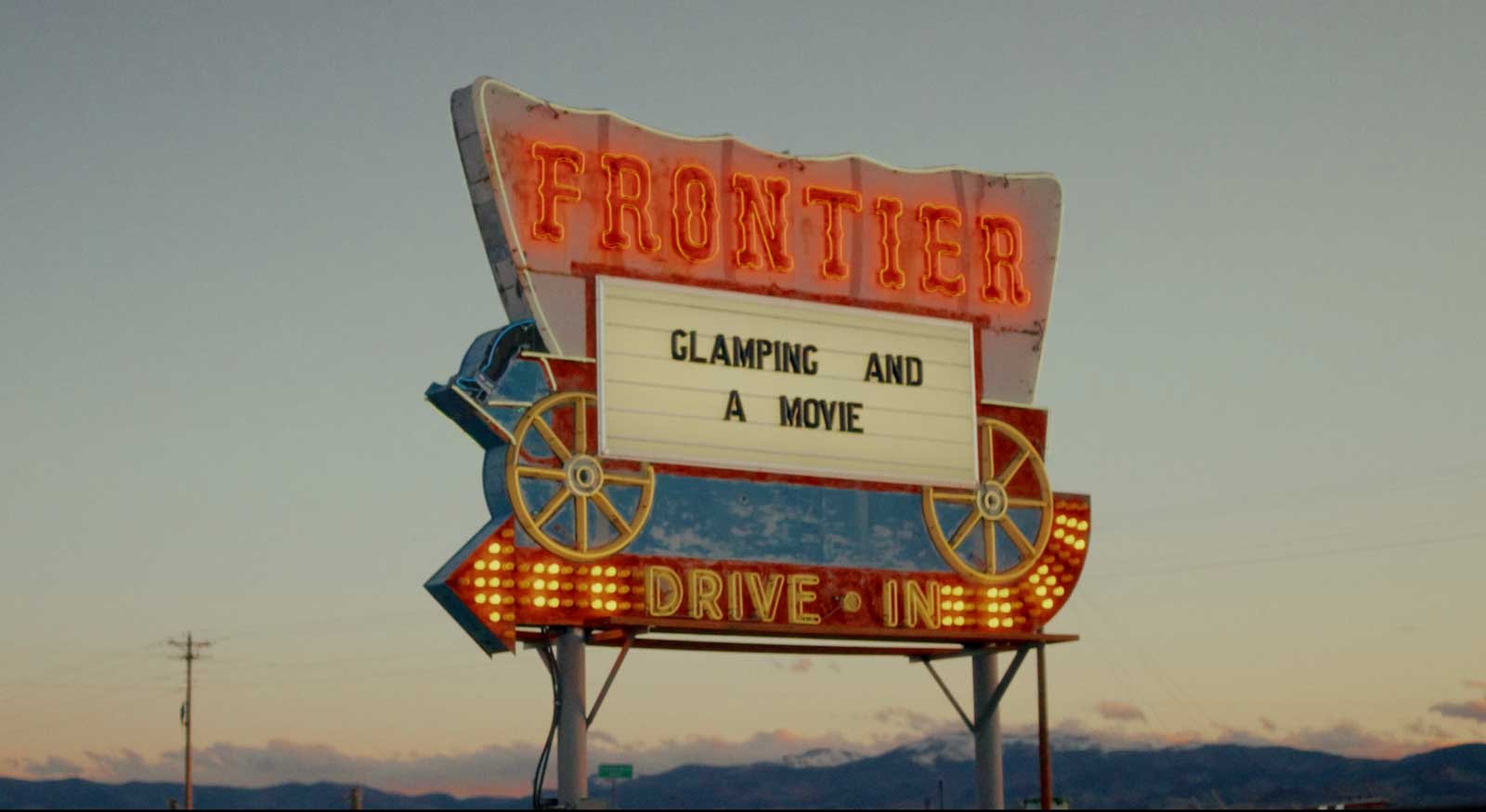 A vintage marquee sign in the shape of a Conestoga wagon glows red and yellow outside the Frontier Drive-Inn near Del Norte, Colorado.