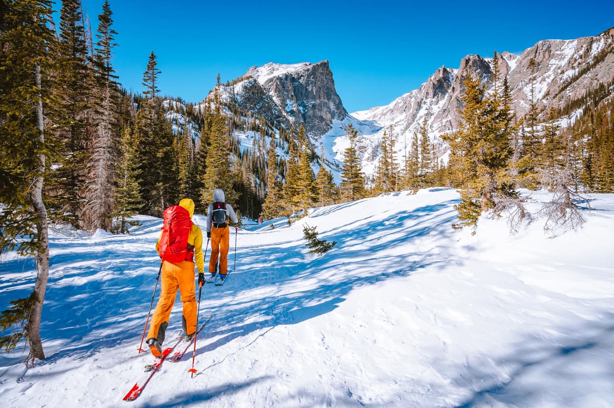Two people backcountry ski across snowy terrain with icy mountains in the background in Estes Park, Colorado.