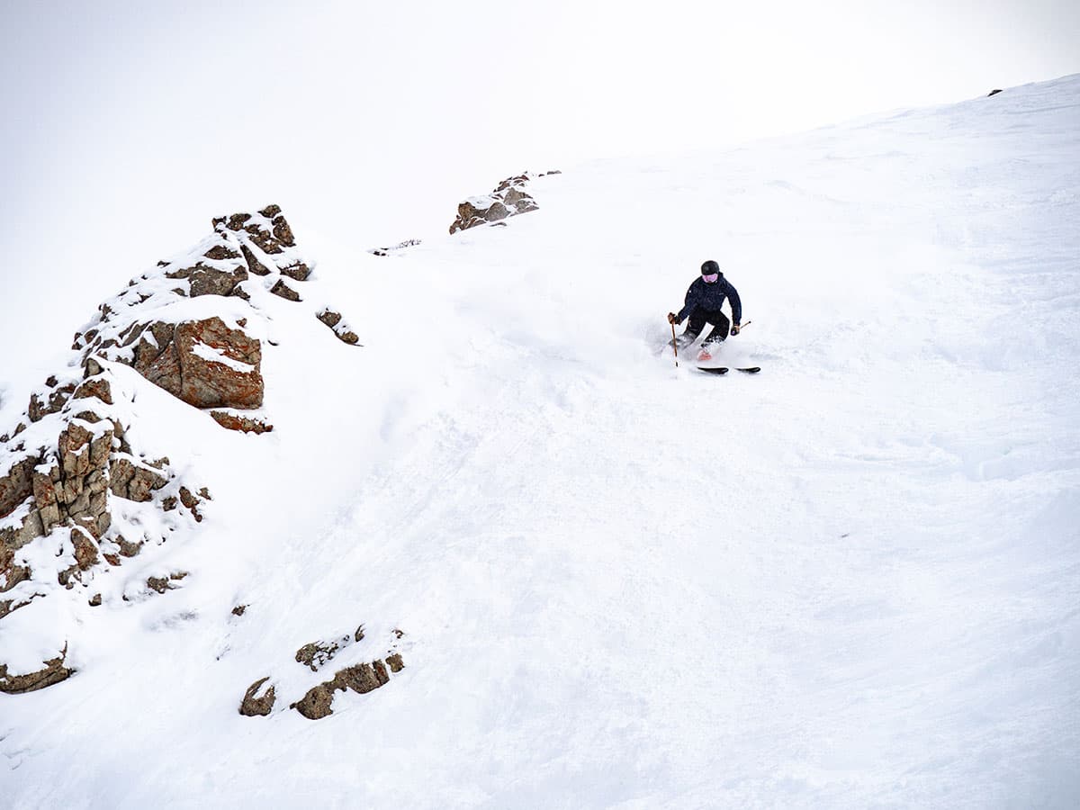 Solo skier on a very steep, snowy ridge alongside jagged rocks