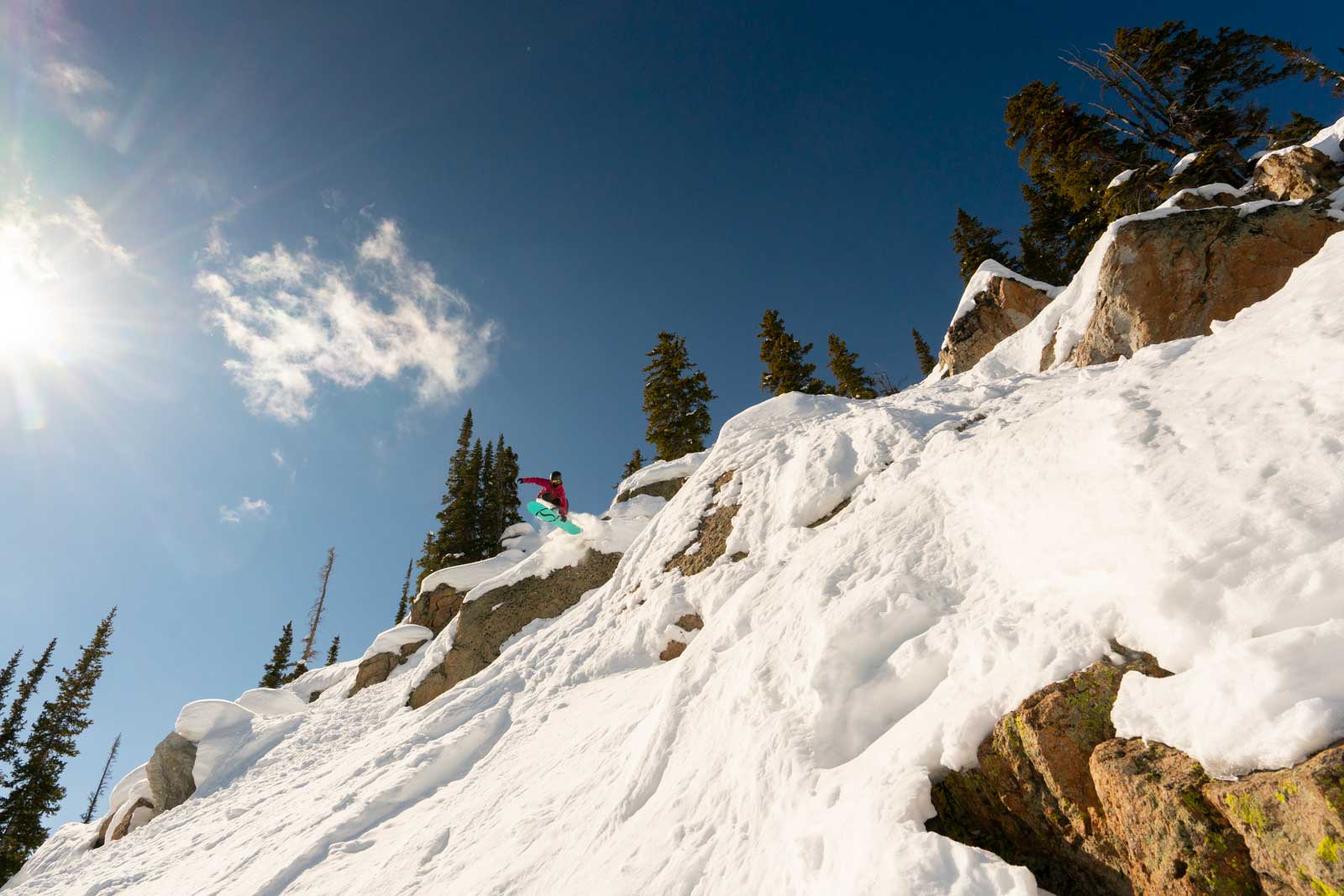 Under a blue sky, a snowboarder takes the plunge into some of Crested Butte Mountain Resort’s steep, technical extreme terrain