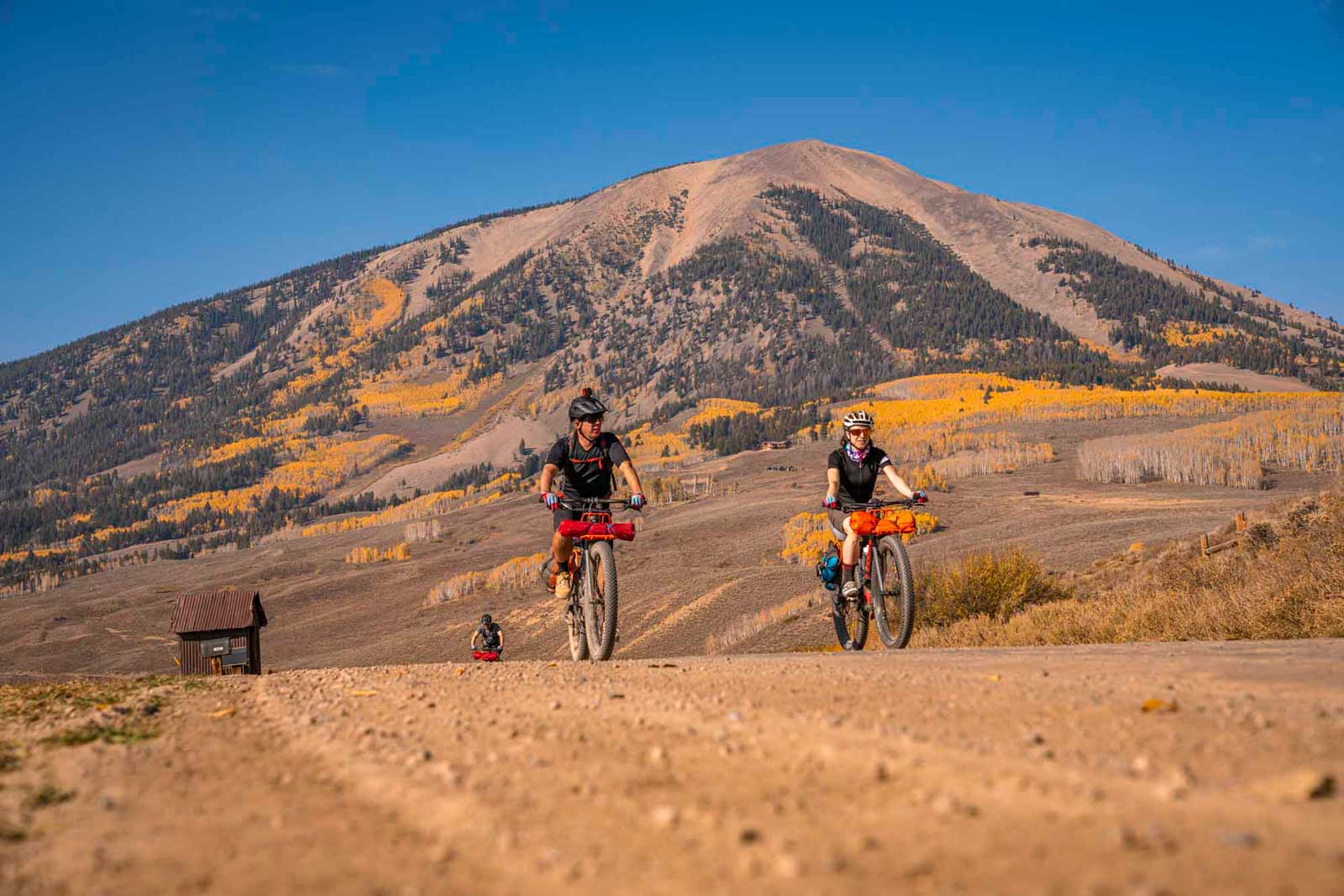 Gravel bikers crest a hill surrounded by the oranges and golds of fall foliage