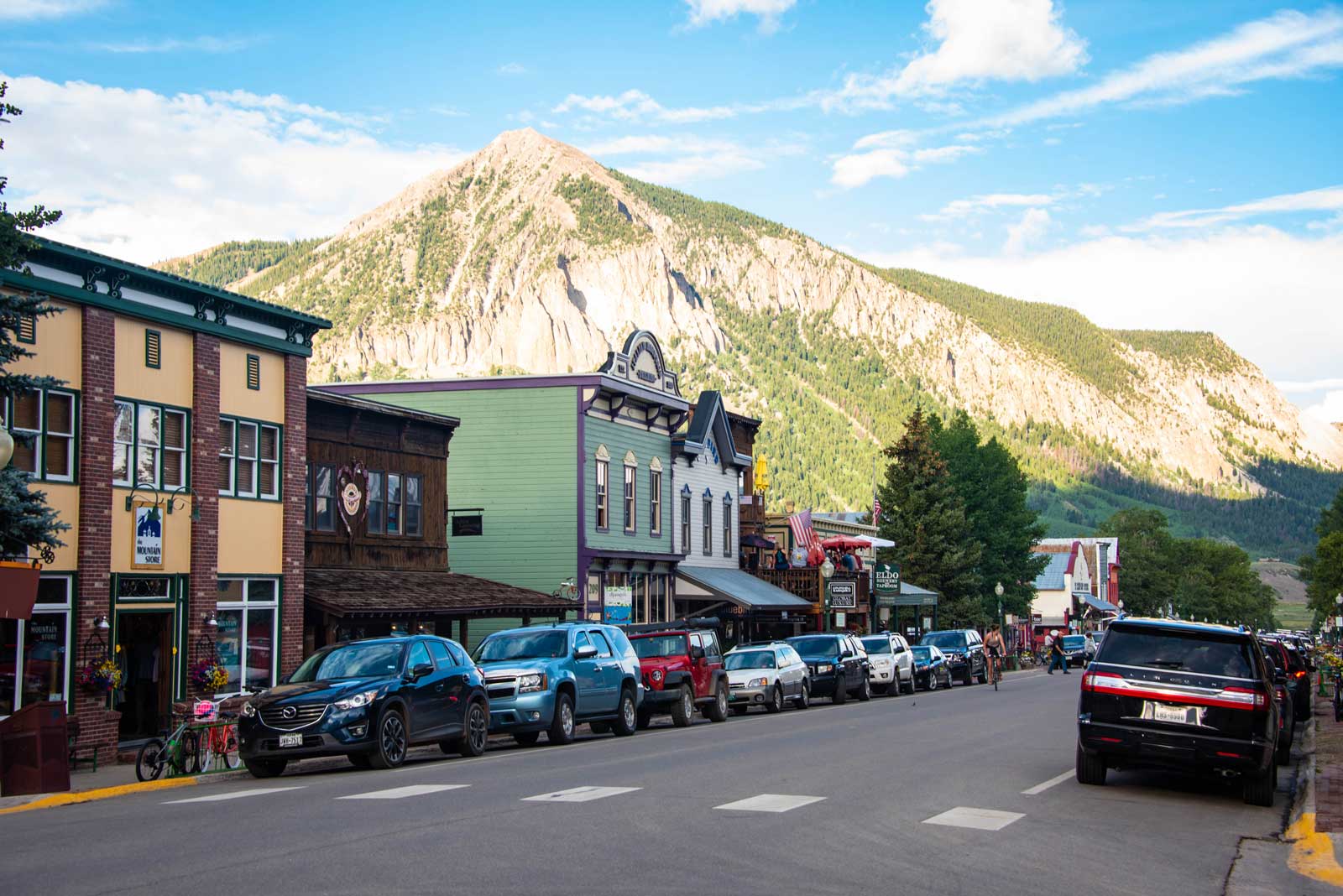 Mount Crested Butte is lit by the sun, with the colorful storefronts of Crested Butte's main street in the shadow below