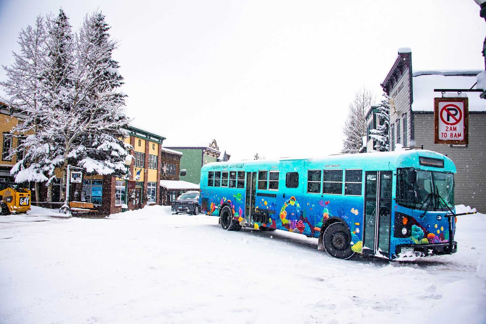 A bright blue Mountain Express town shuttle drives down Elk Avenue in the snow