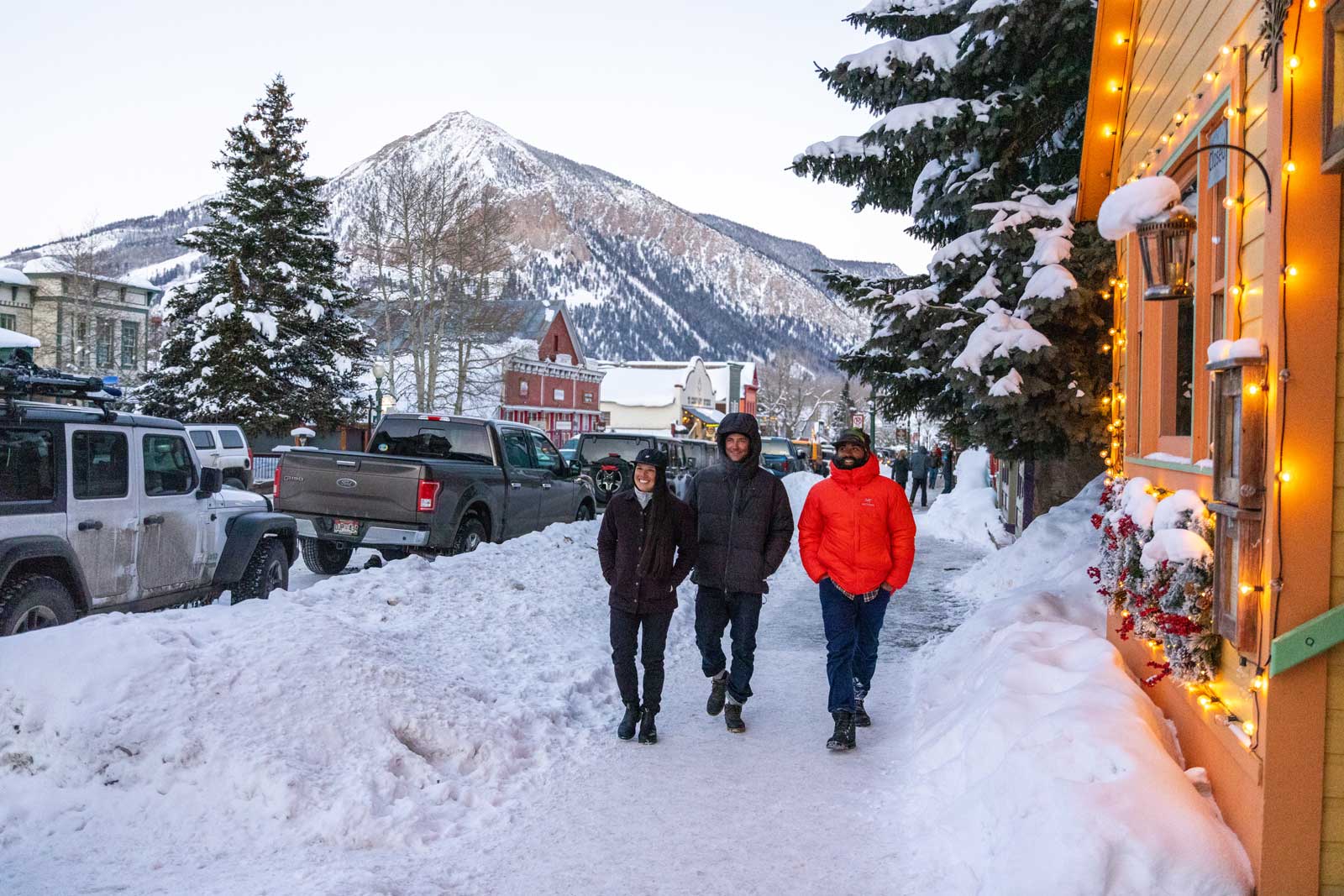 Three people bundled up walk down a snowy street lined with shops in Crested Butte