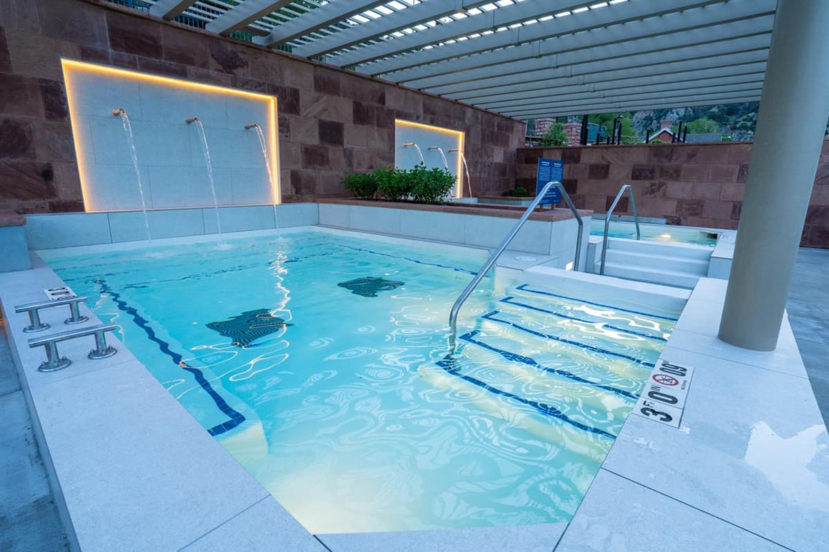 A hot-springs pool appears blue in the soft lighting at Glenwood Hot Springs Resort. A water feature utilizes three bronze pipes to pour fresh water into the pool.