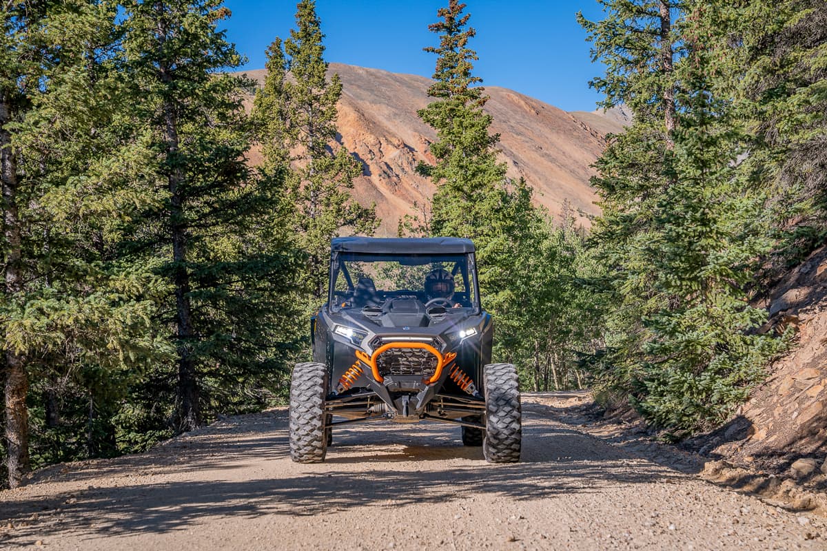 A side-by-side rides on a forested trail with mountains in the background in Crested Butte and Gunnison Colorado.