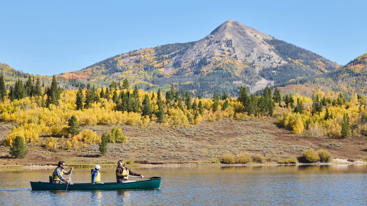 Family canoeing on Pearl Lake near Steamboat Springs, surrounded by fall-colored trees and mountains in the background.
