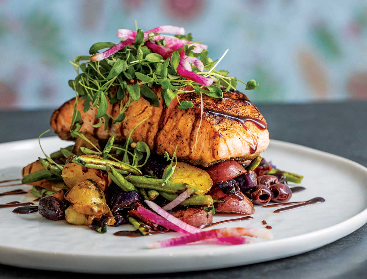 Freshly grilled fish sits atop a bed of veggies and pickled pink onions