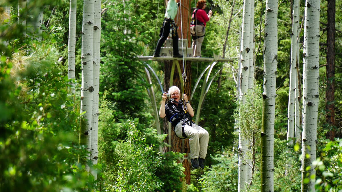 Person taking pictures while ziplining through aspen trees, surrounded by greenery in the San Juan National Forest.