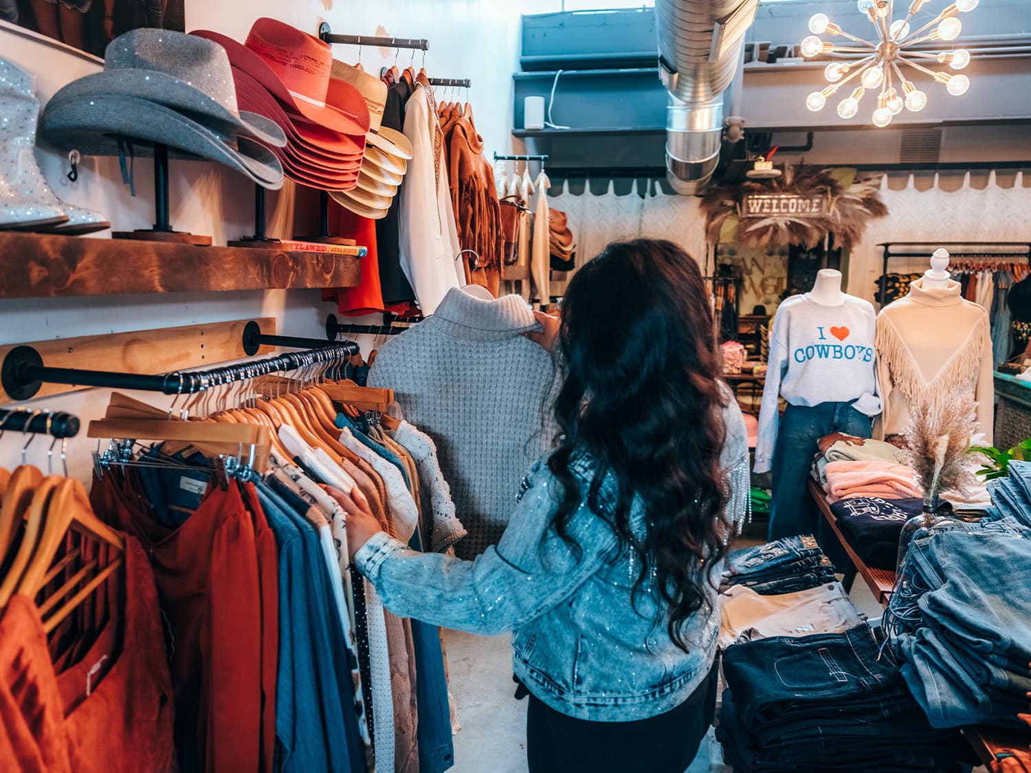 A person combs through racks of sweaters, cowboy hats and blouses at Urban Cowgirl boutique in Aurora, Colorado.