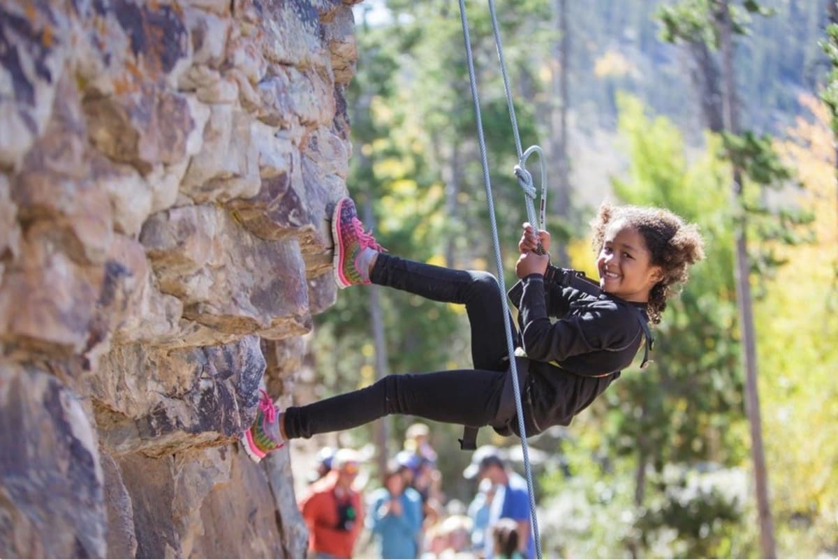 A smiling child rappels down a rock face on an outing with Colorado Adventure Guides