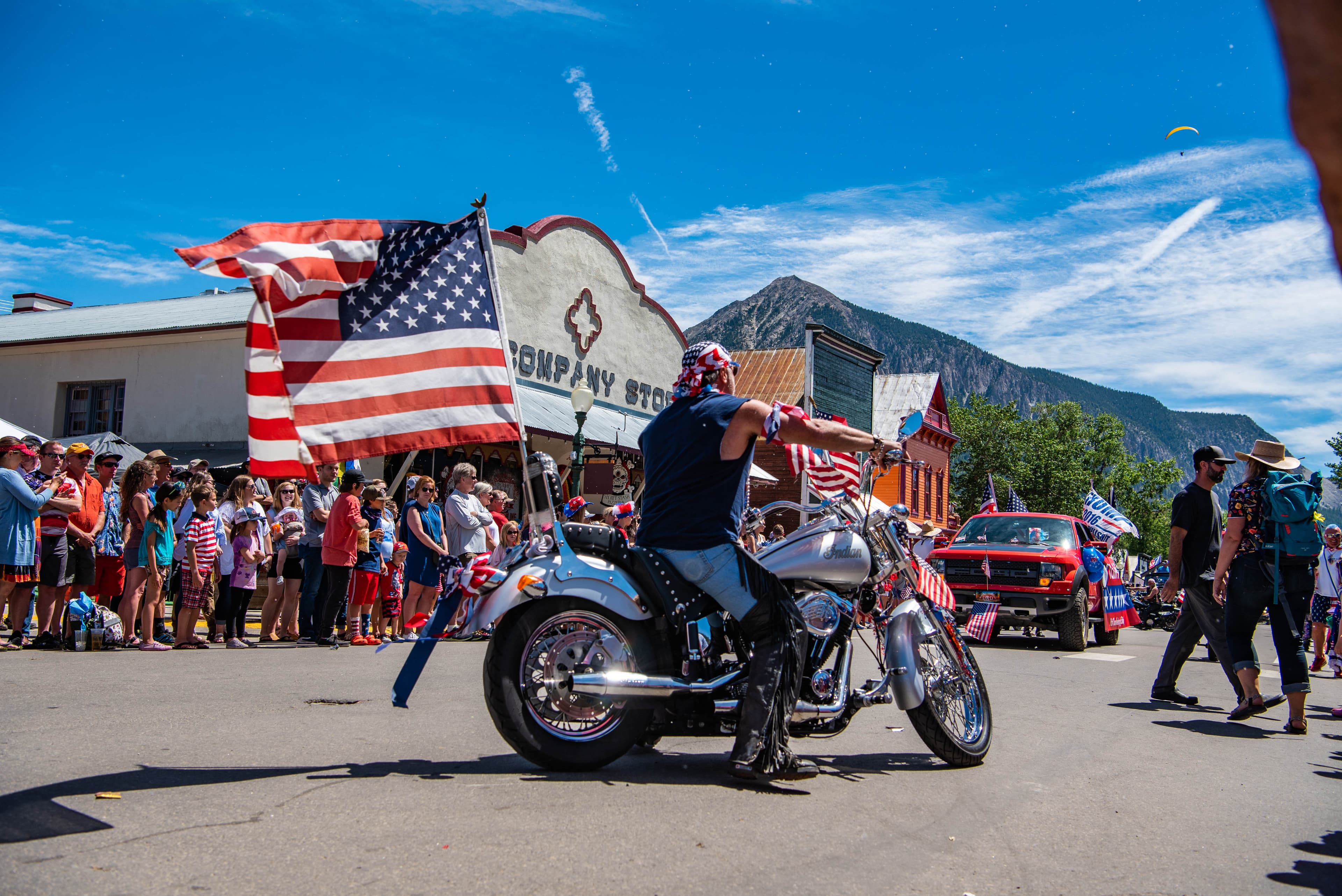 Fourth of July parade in Crested Butte with people lining the street and a motorcyclist carrying an American flag.