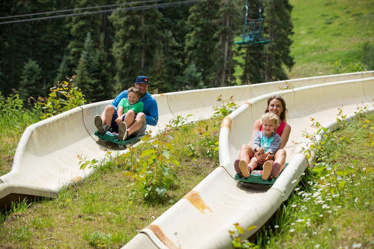 Family laughing while rising down the alpine slide on a summer day at Purgatory Resort in Durango.