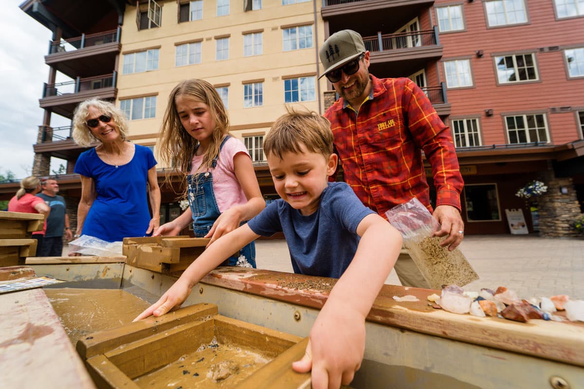 Family gem panning for treasures at Purgatory Resort, with a kid sifting through sand.