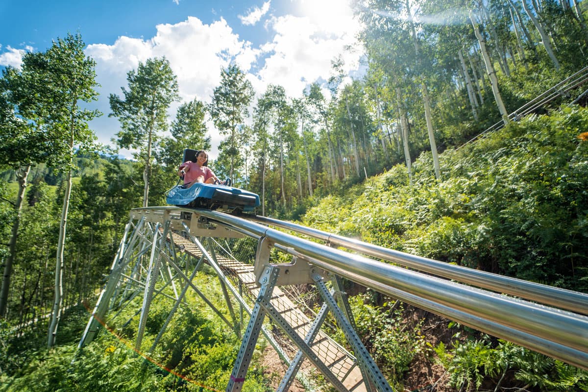A girl riding the mountain coaster at Purgatory Resort, preparing to head downhill through the trees.