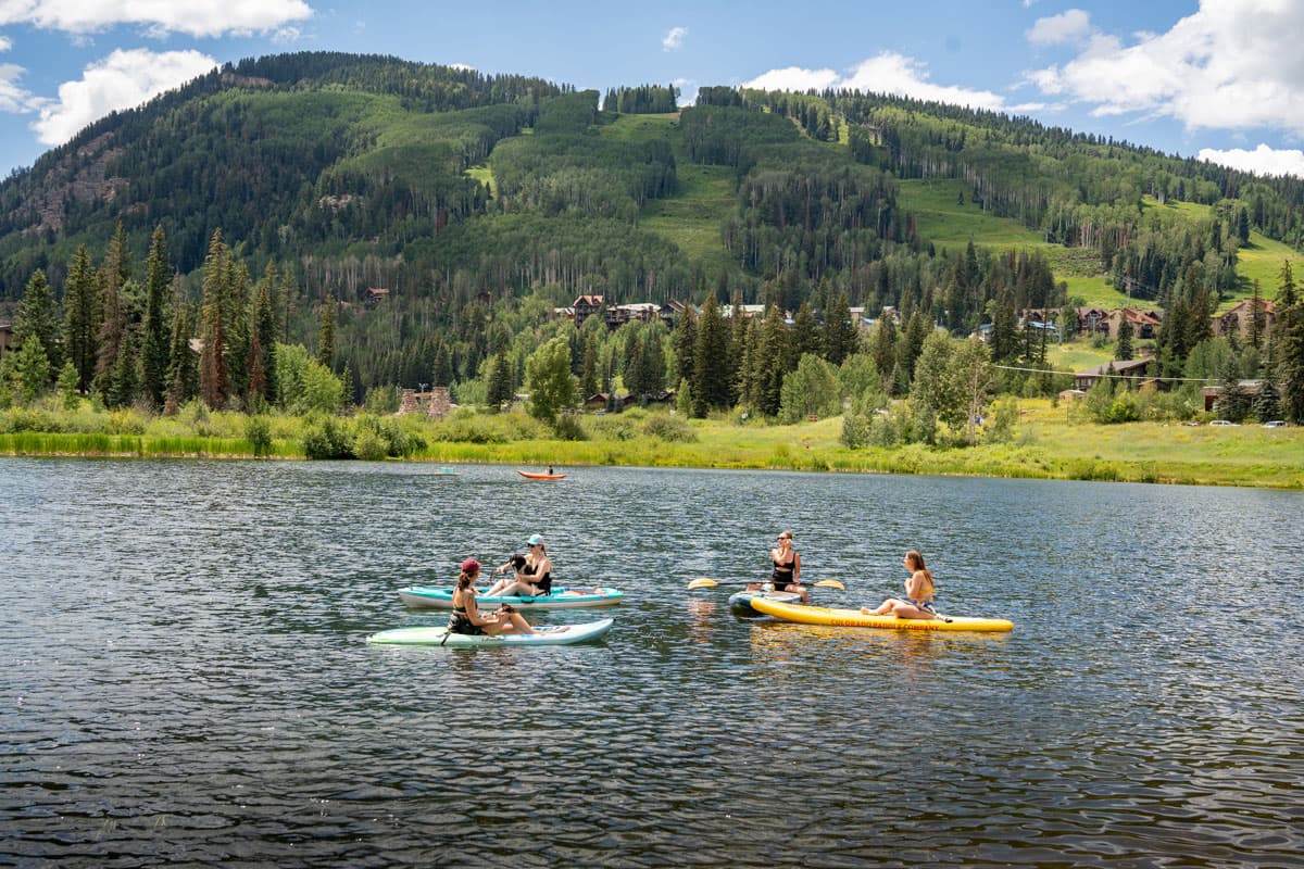 Friends paddling across a still lake with greenery and rolling slopes in the background.