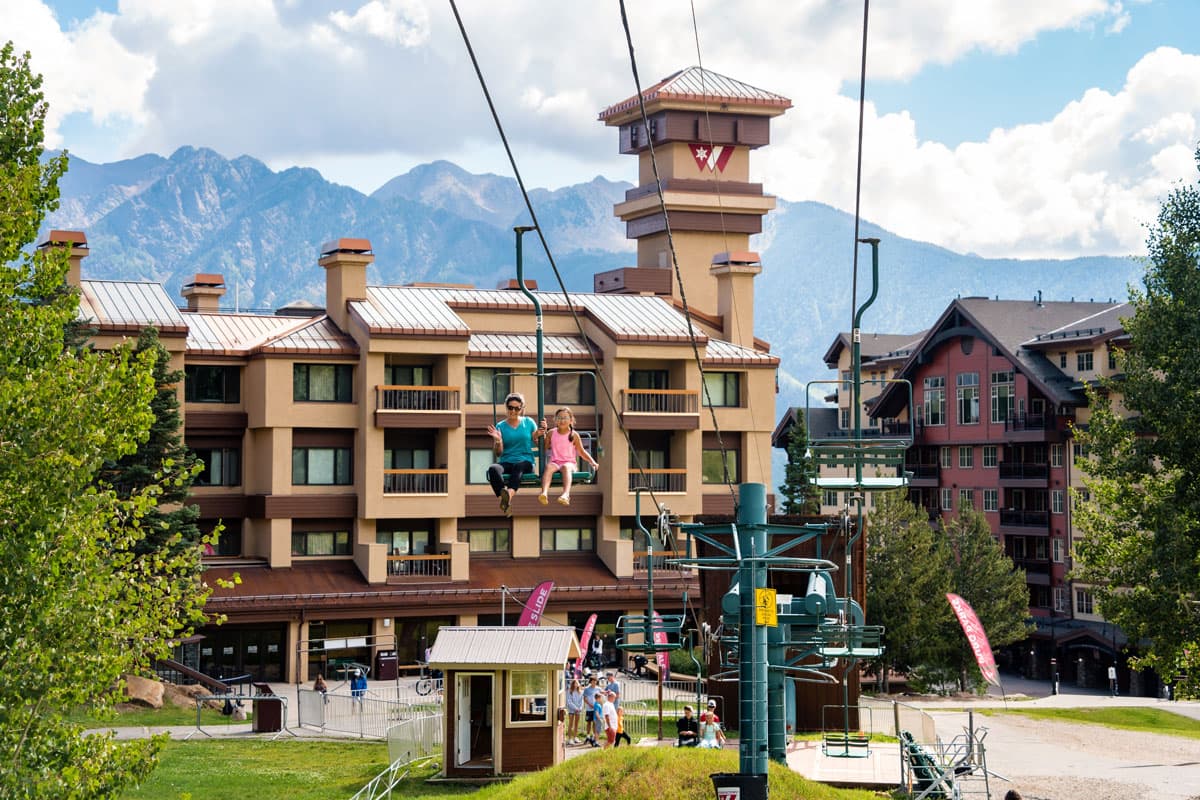 Mother and daughter riding a chairlift, ascending toward the sky with Purgatory Resort in the background.