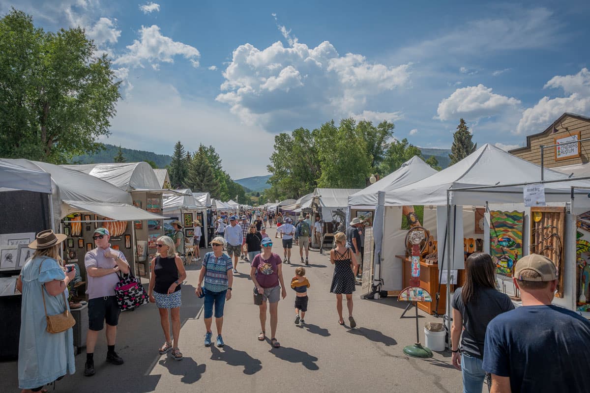 People shopping at the Crested Butte Arts Festival with white tents lining the street.