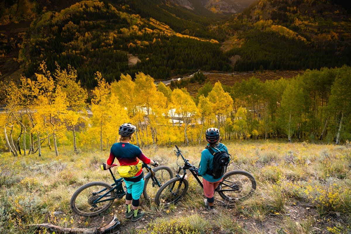 Two people standing aside their mountain bikes and admiring the view below them of the fall-colored landscape in Crested Butte, Colorado.