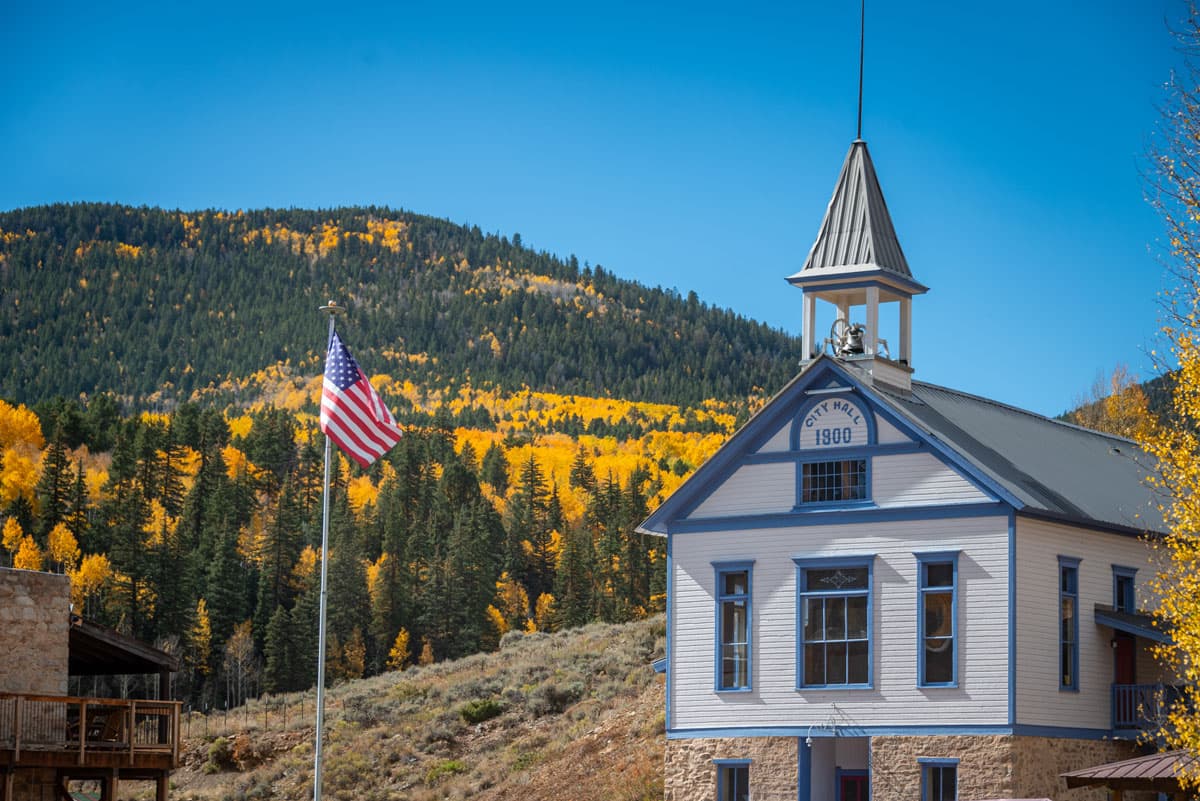 White and blue colored City Hall with scenic hillside aside it in Pitkin, Colorado.